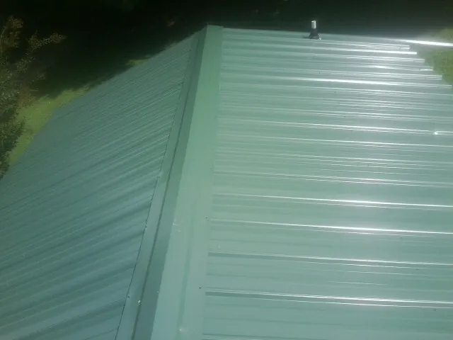 New green metal panels meeting at the ridge of a roof — Flat Roof Repair work by our crew in Beloit