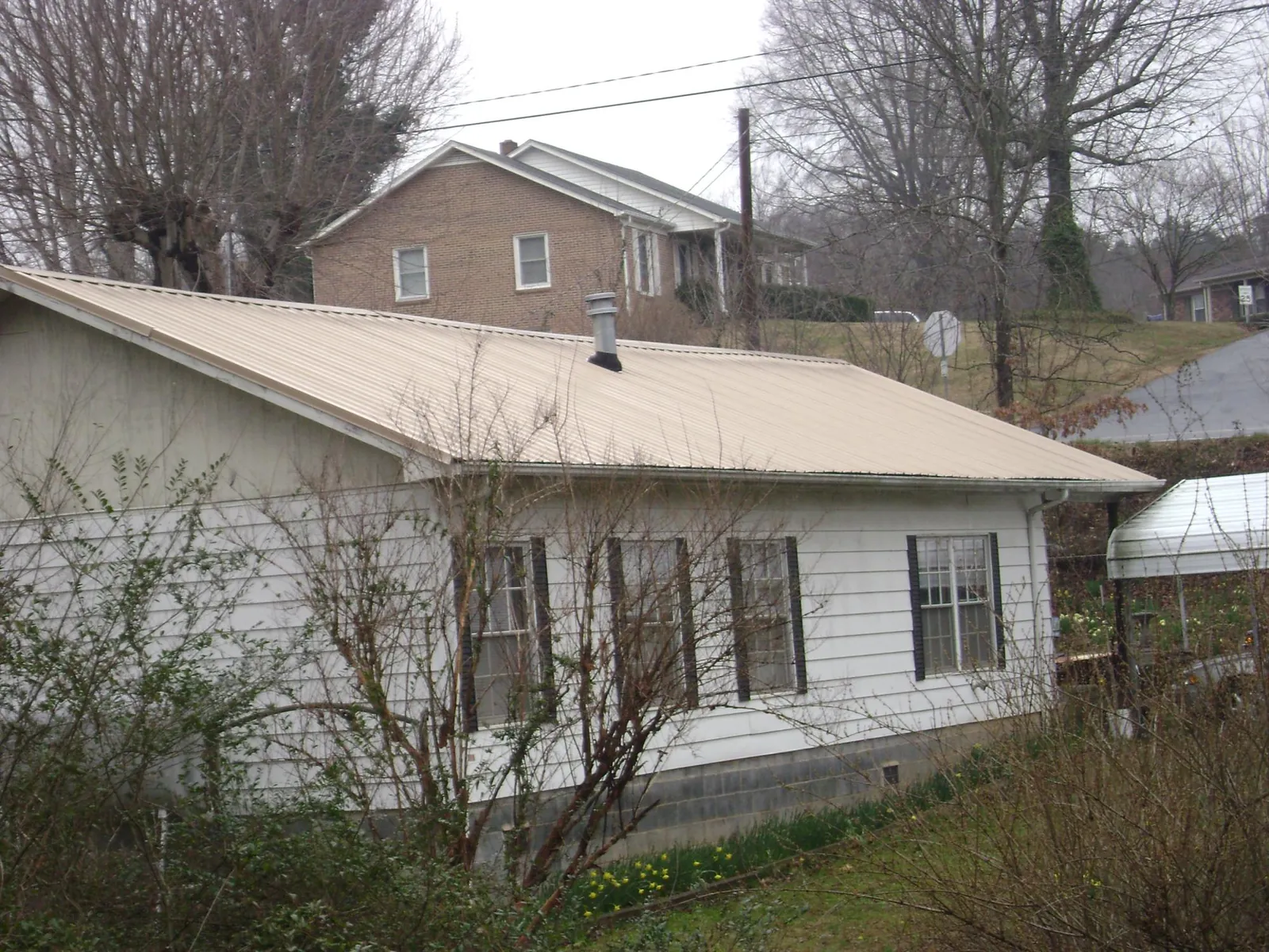 Tan metal roof on a white sided house set into a hillside — Commercial Roofing by Roofing Brothers in Beloit