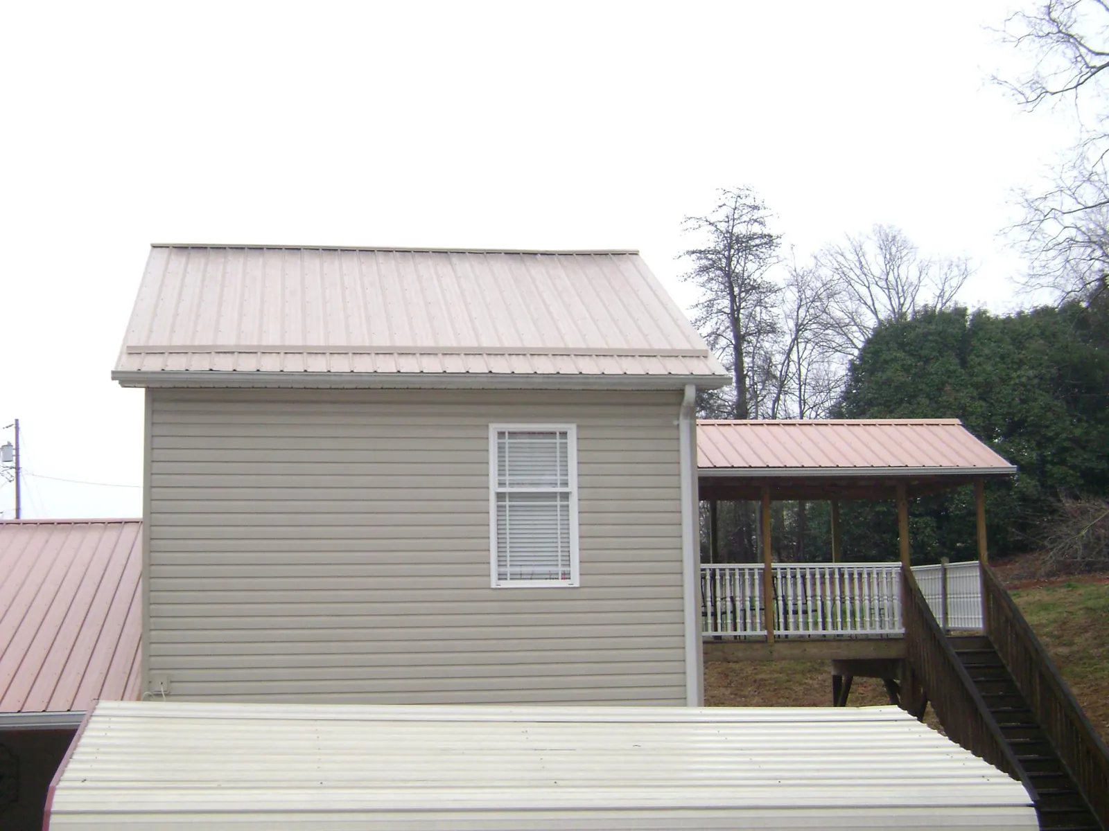Tan metal roofs on a two story addition and attached porch, from a Roof Replacement job in Beloit